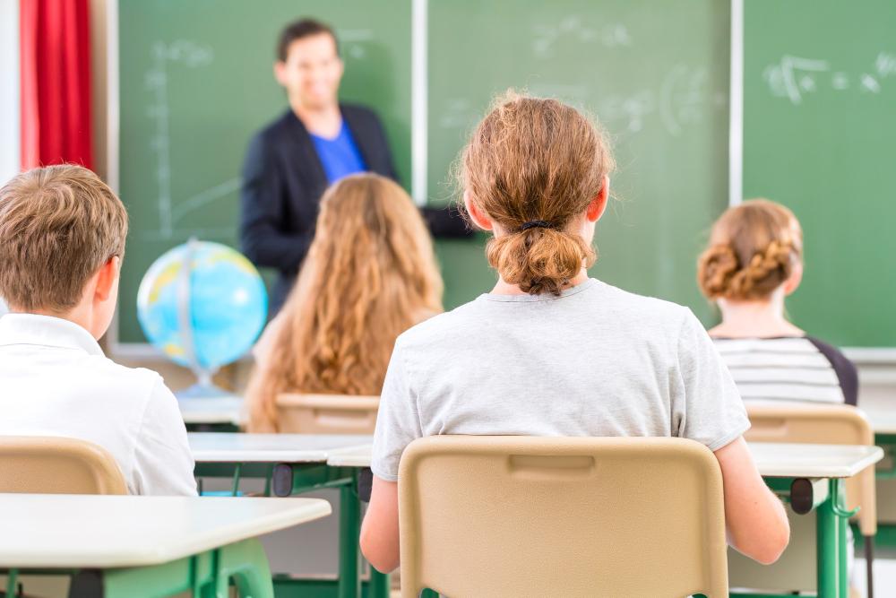 Teacher in front of blackboard teaching to students in a classroom.